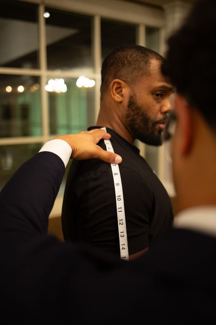 A tailor measuring a client across the shoulder with a tape measure